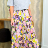 Woman wearing a light blue top and colorful floral skirt indoors.