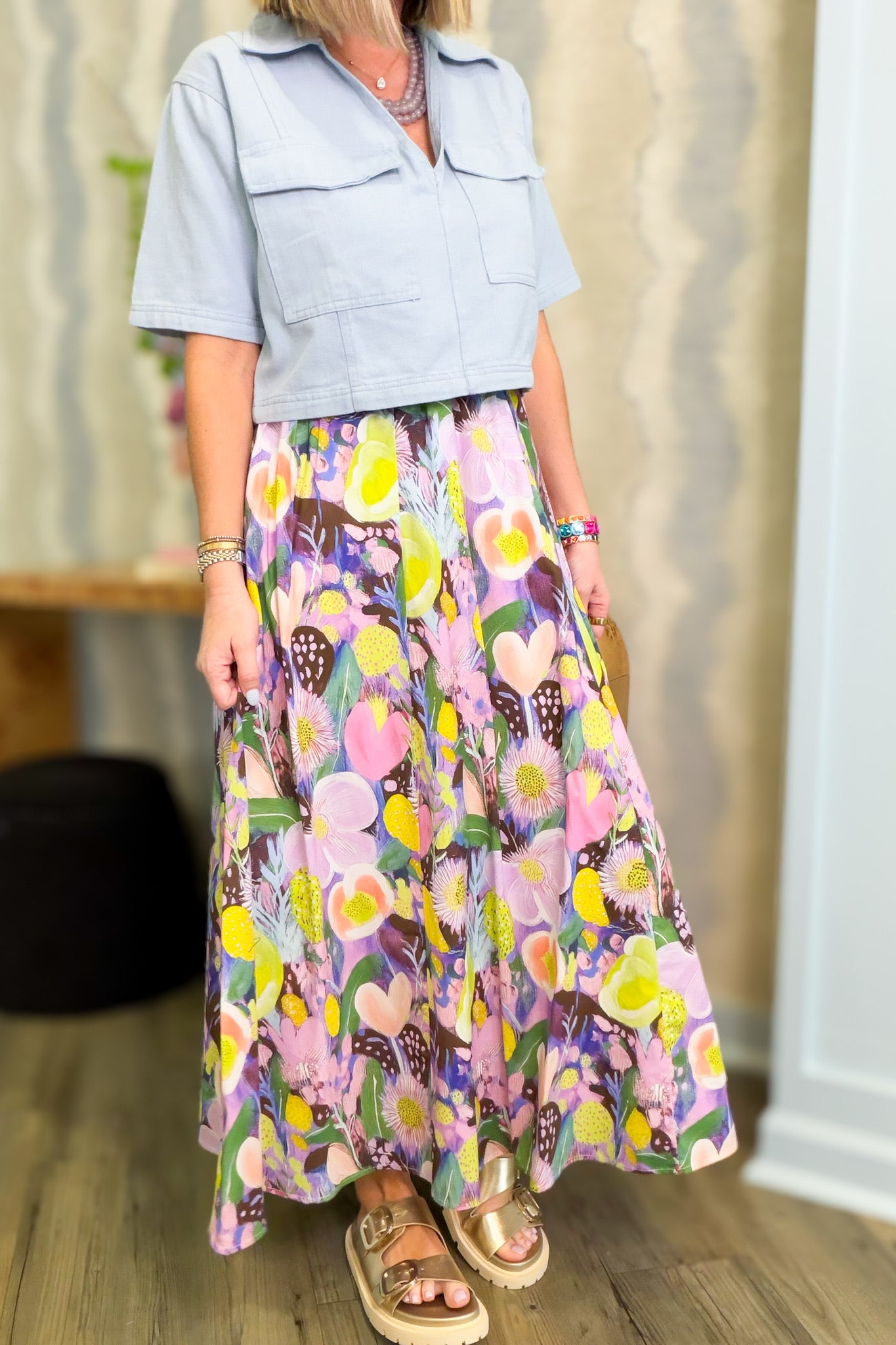 Woman wearing a light blue top and colorful floral skirt indoors.